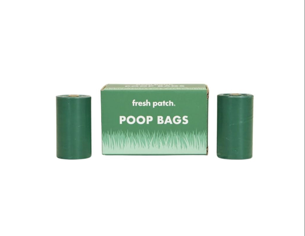 Two green poop bag rolls are standing to the two sides of a box labeled "fresh patch Poop Bags"