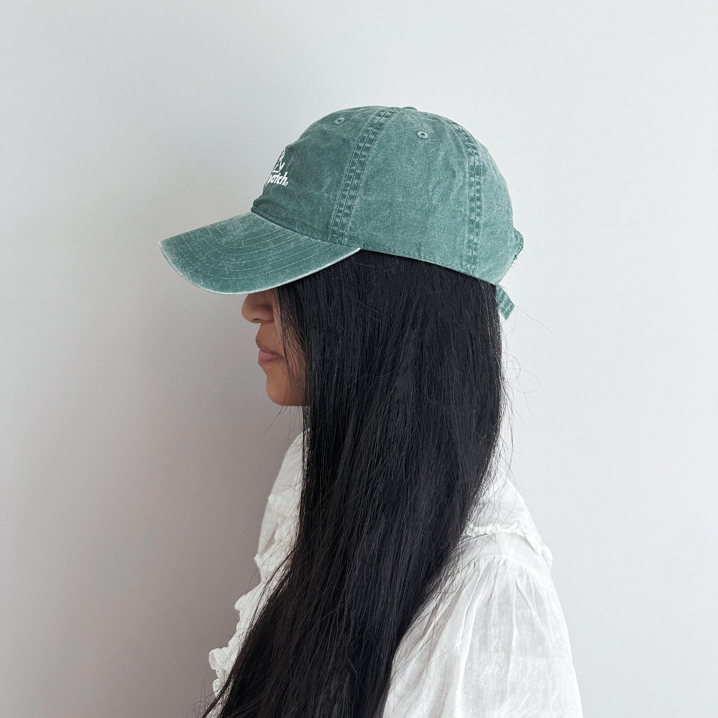 Girl with long black hair wearing greenish baseball cap facing to the left