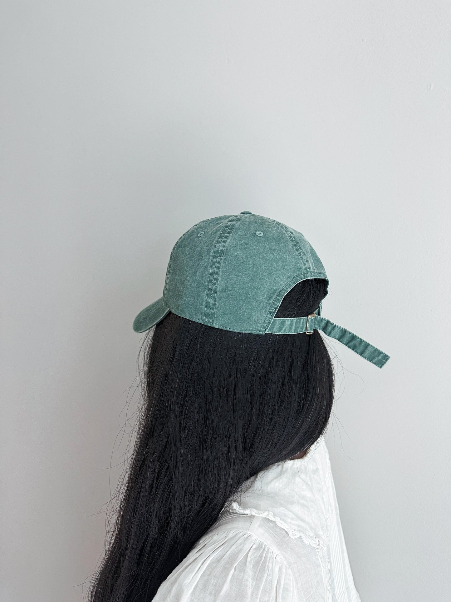 Girl with long black hair wearing greenish baseball cap turned away