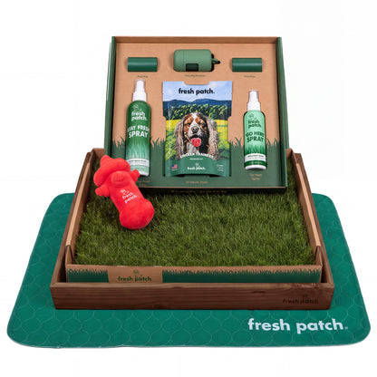Fresh Patch potty training kit with a real grass tray in a dark wooden frame, a plush hydrant toy, two sprays, dog treats, poop bags and a green pad.
