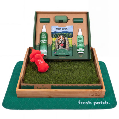 Fresh Patch potty training kit with a real grass tray in a wooden frame, a plush hydrant toy, two sprays, dog treats, poop bags and a green pad.