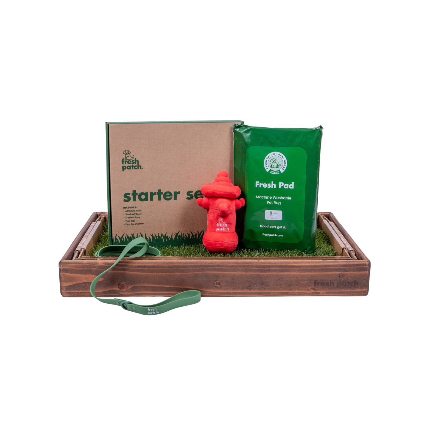 Dog training kit with cardboard box, green bag, red fire hydrant toy, and grass patch in a wooden tray.